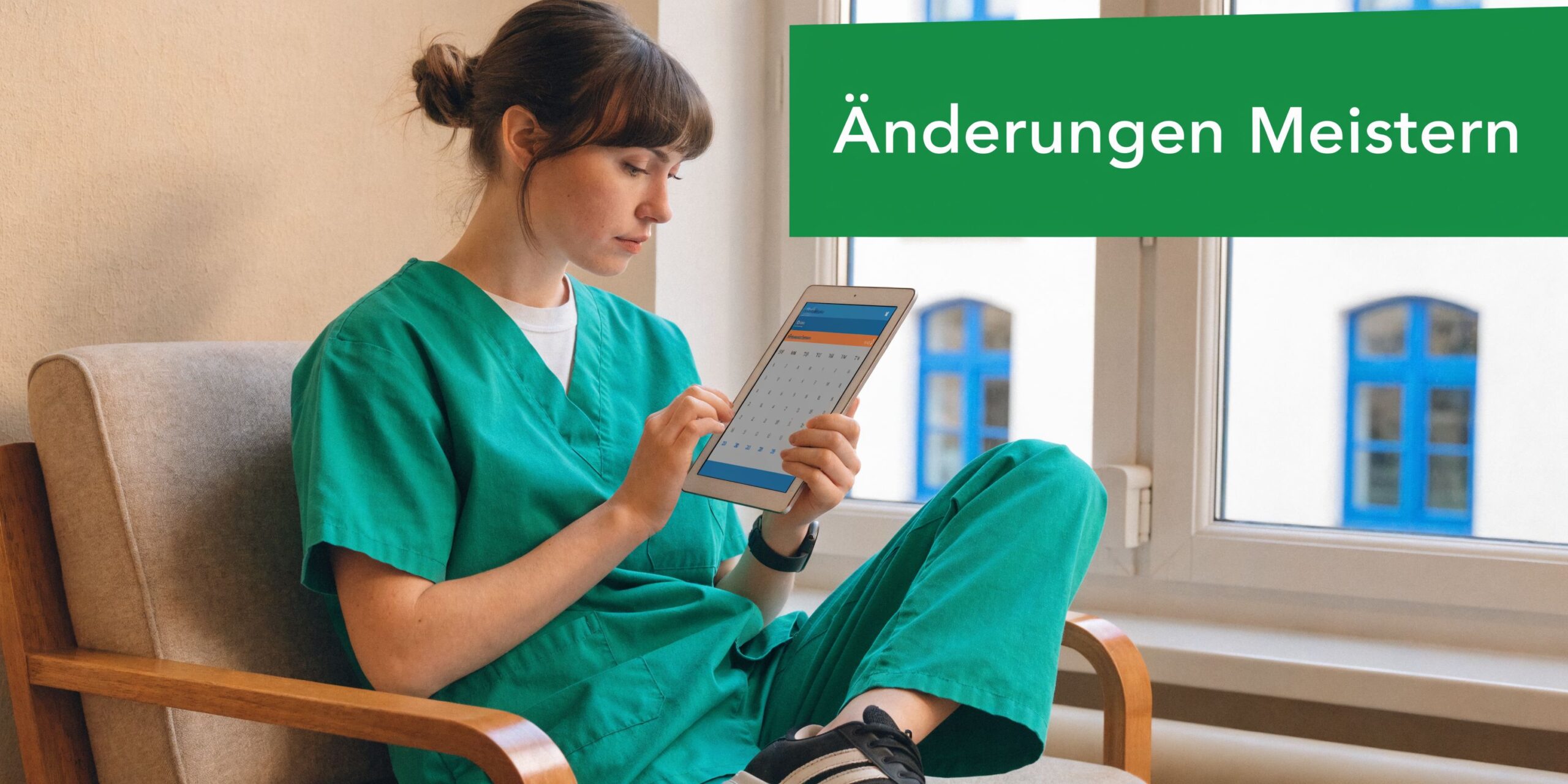 Eine Pflegekraft in grüner Arbeitskleidung sitzt in einem Sessel und plant Dienstpläne auf einem digitalen Tablet.