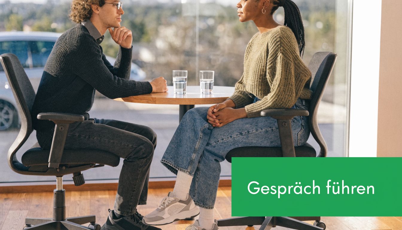 Ein Mann und eine Frau sitzen sich gegenüber an einem Tisch und führen ein berufliches Gespräch.