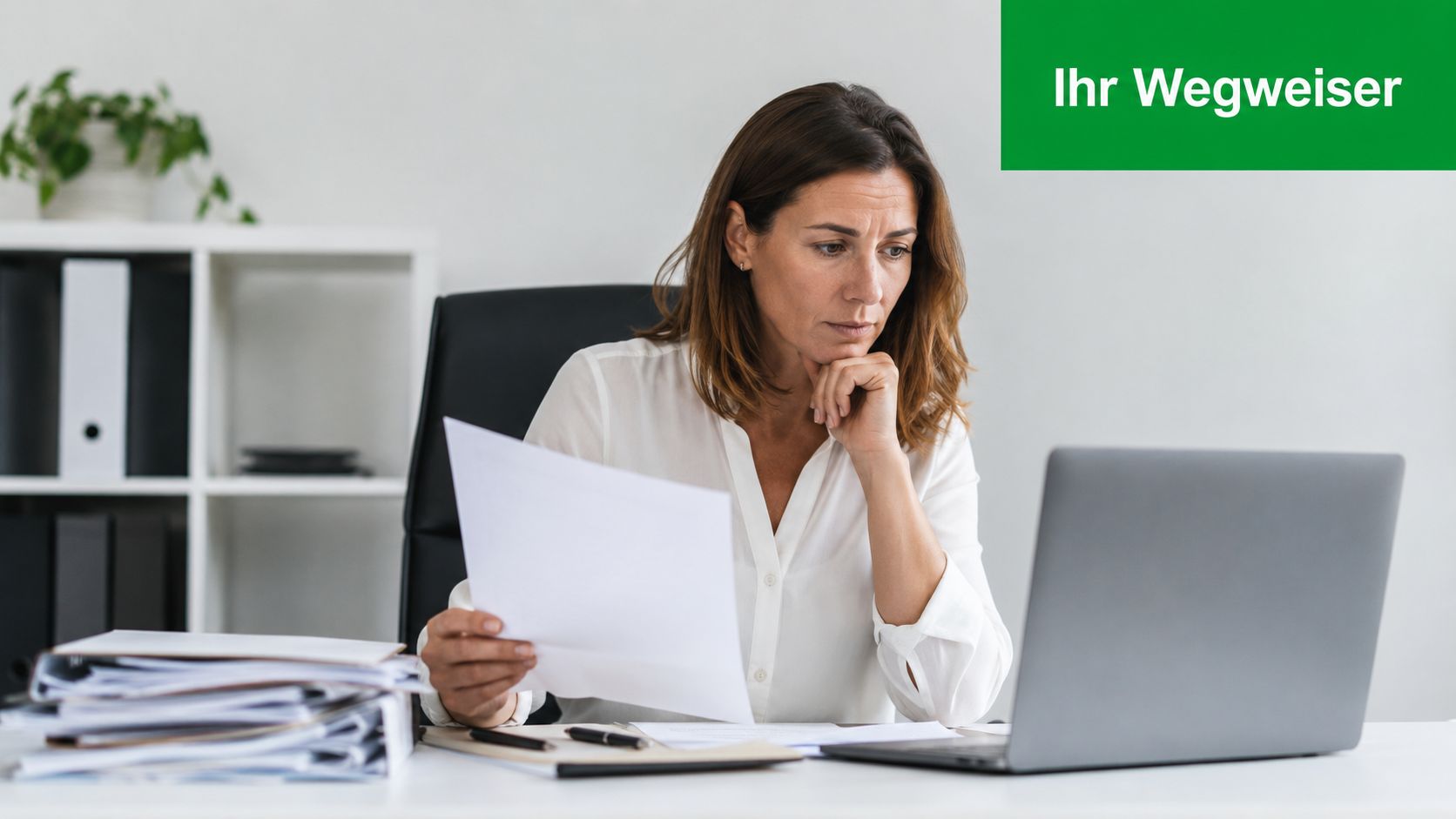 Eine konzentrierte Frau in einer weißen Bluse arbeitet an ihrem Schreibtisch mit Dokumenten und einem Laptop.