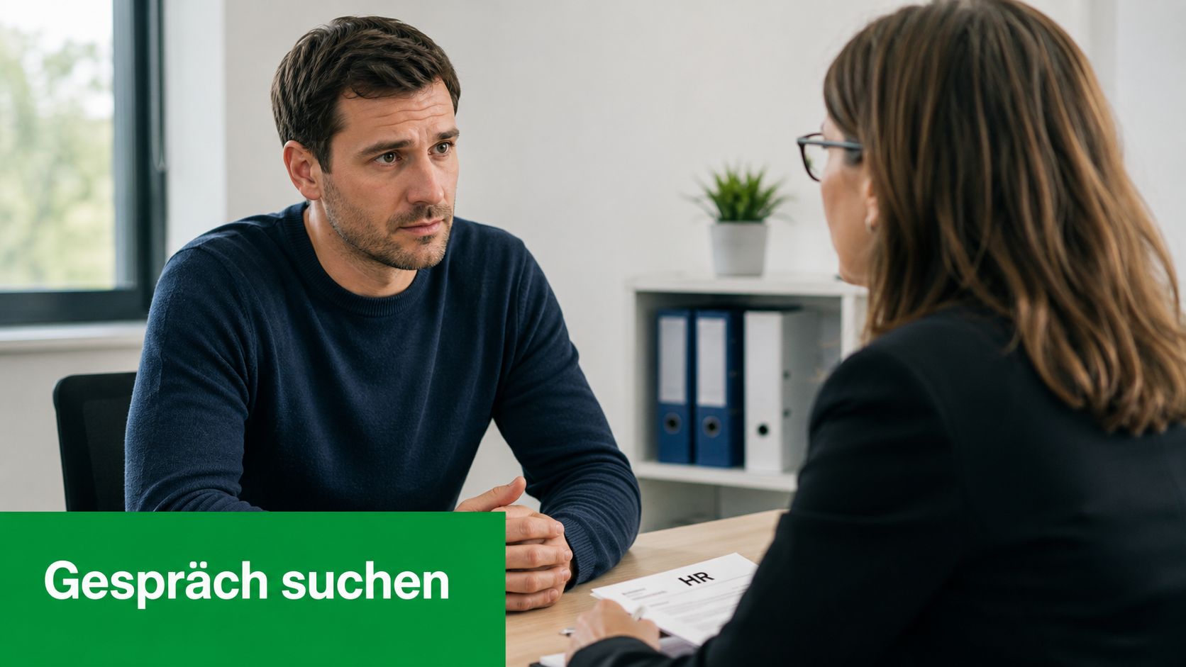 Ein Mann im Gespräch mit einer Person aus der Personalabteilung an einem Schreibtisch im Büro.