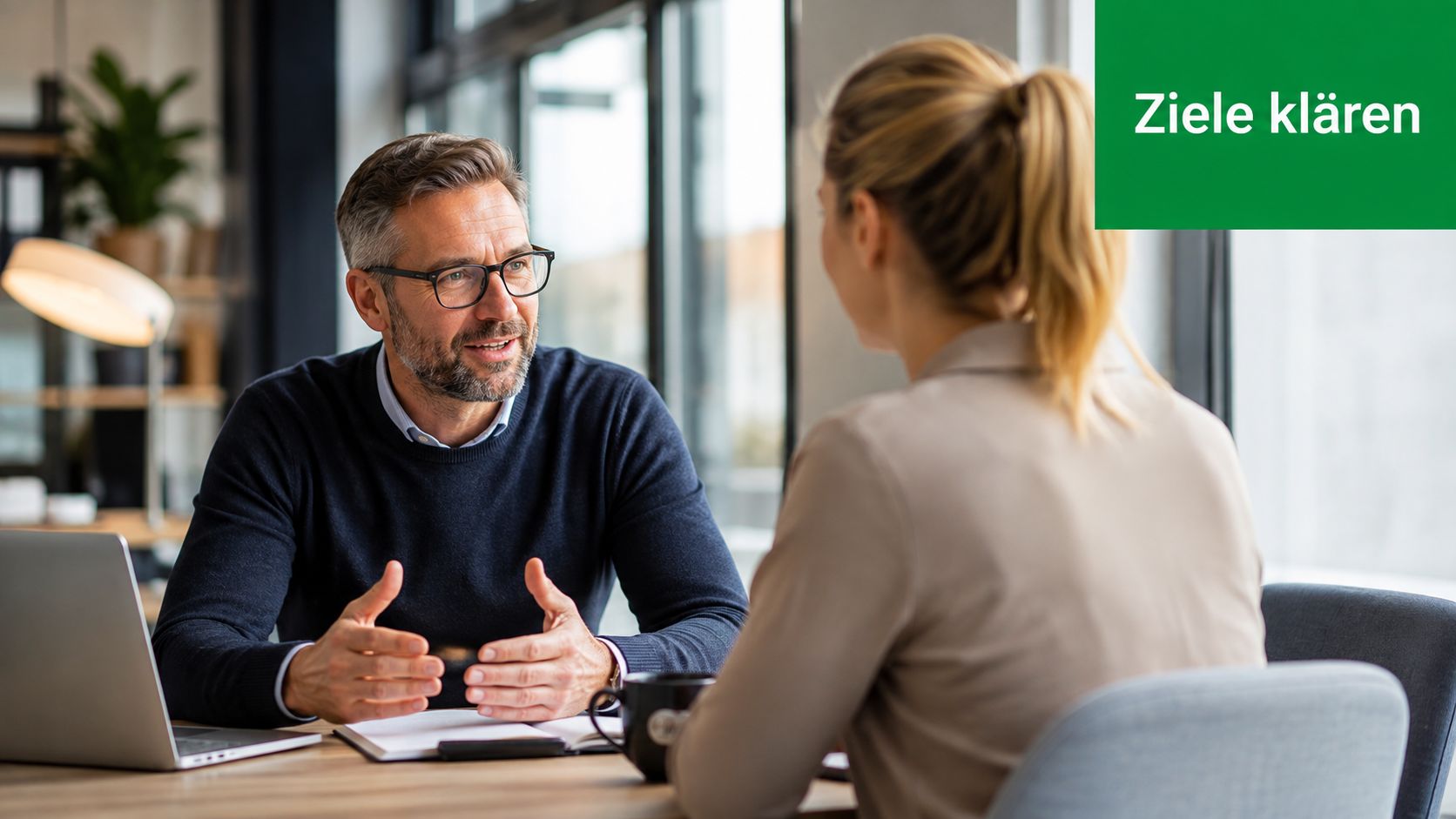 Ein Mann mit Brille und eine Frau im Gespräch während eines Meetings in einem modernen Büro.